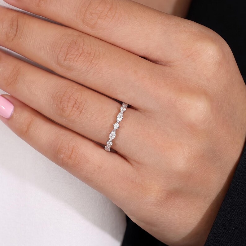 A delicate marquise and round diamond wedding ring worn on a woman's finger with a light-colored sleeve visible. The slim polished band displays an alternating gemstone arrangement across the front. This elegant lab grown diamond ring combines a minimalist silhouette with subtle sparkle, making it suitable for stacking, bridal jewelry and everyday wear.