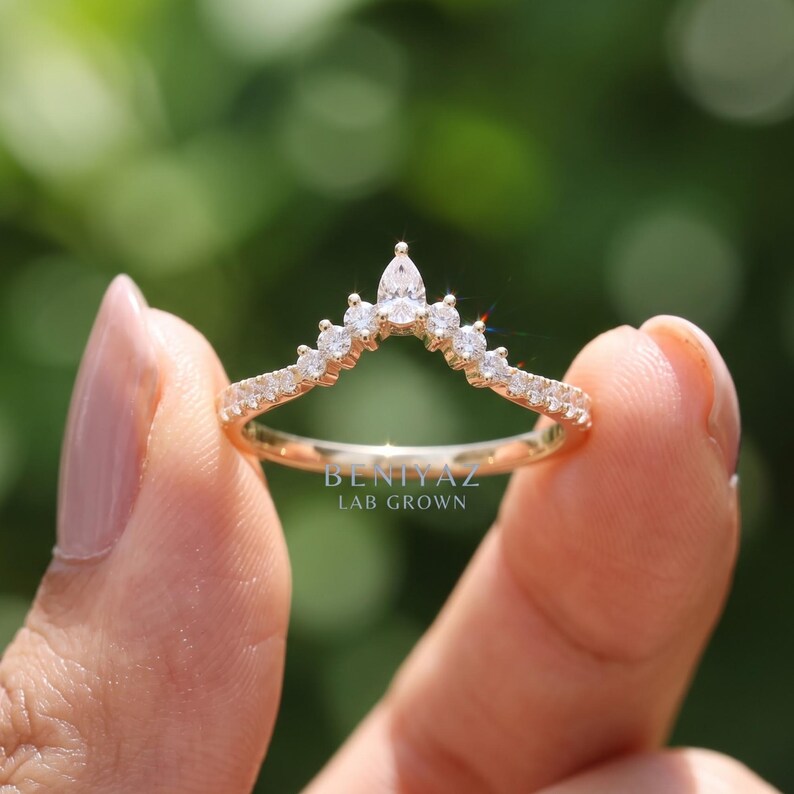Hand holding a yellow gold curved diamond wedding band featuring pear and round lab grown diamonds, designed as a chevron nesting and stacking ring