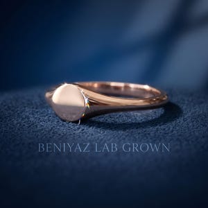 Side profile of plain round signet ring on blue background showing thin tapered band and rose gold tone high polish finish