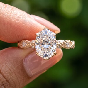 Hand wearing a vintage oval lab grown diamond engagement ring in rose gold with marquise accent stones and detailed milgrain band design