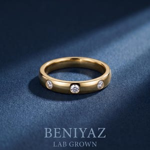 May include: A gold band ring featuring three flush-set round clear stones spaced evenly along the outer surface. The text BENIYAZ LAB GROWN is printed in white at the bottom of the frame, centered below the ring.