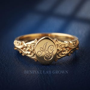 Personalized initial signet ring in yellow gold with decorative script monogram engraving on the oval face.