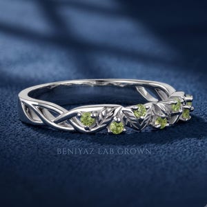 Close up of a peridot wedding band featuring round green stones, leaf motifs and flowing vine details.
