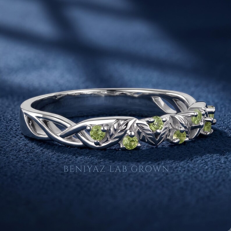 Close up of a peridot wedding band featuring round green stones, leaf motifs and flowing vine details.