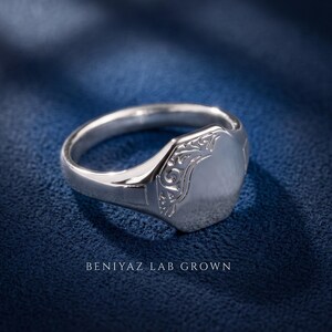 Sterling silver oval signet ring on blue background with high polish engraving face, floral scrollwork shoulders and tapered band