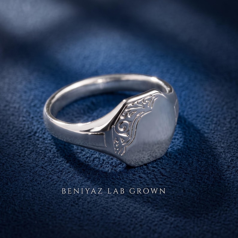 Sterling silver oval signet ring on blue background with high polish engraving face, floral scrollwork shoulders and tapered band