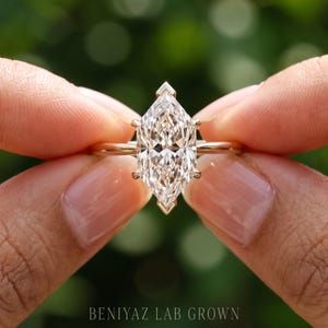 Op de afbeelding: Een ring met een marquise-geslepen diamant, een heldere, gefacetteerde steen, gezet in een gouden band met V-vormige zettingen aan de boven- en onderkant. De tekst BENIYAZ LAB GROWN staat onderaan de afbeelding in een schreefloos lettertype.