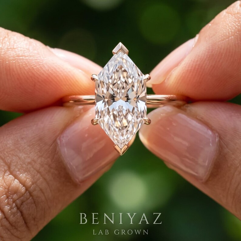 Op de afbeelding: Een solitaire ring met een heldere, gefacetteerde edelsteen in marquise-slijpvorm, gezet in een gepolijste ros&eacute;gouden band. De zetting bevat zes klauwen die de steen aan de boven-, onder- en zijkanten vastzetten. De tekst BENIYAZ LAB GROWN is zichtbaar.