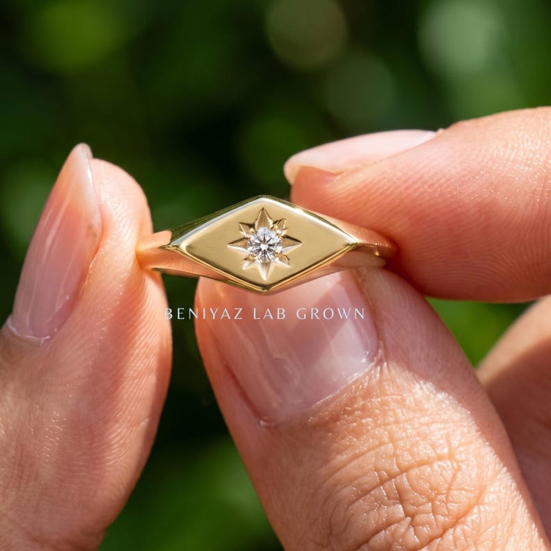 Star set ring close up with single round lab grown diamond, elongated signet face and minimalist yellow gold design.