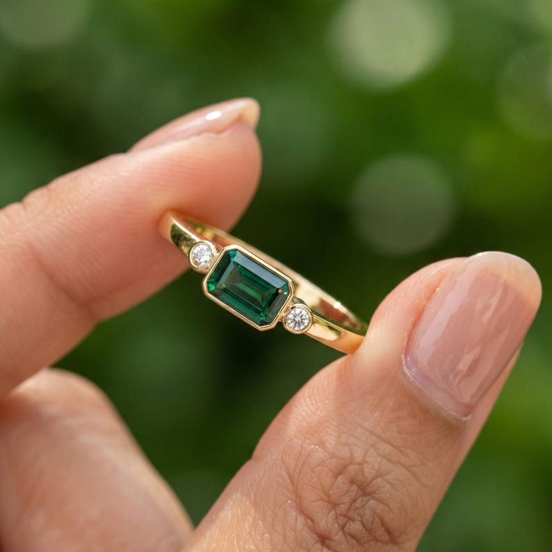 Side angle of east west emerald ring showing the horizontal green lab grown emerald, solid gold band and diamond accent setting.