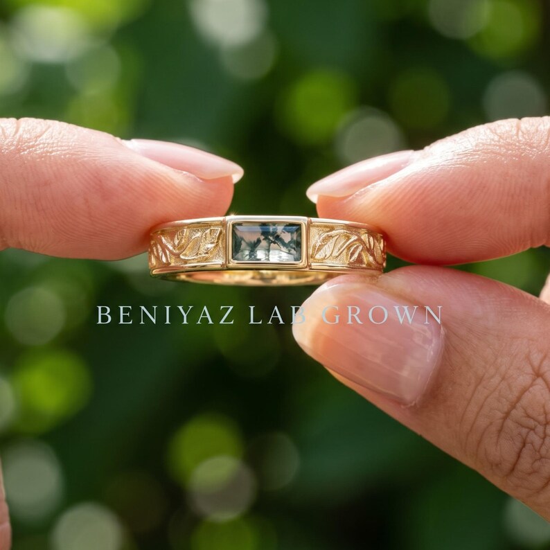 Puede incluir: Un anillo de oro con una piedra de &aacute;gata musgosa rectangular de corte baguette en el centro. La banda est&aacute; decorada con un patr&oacute;n de hojas en relieve detallado a ambos lados de la piedra. El texto BENIYAZ LAB GROWN aparece bajo el anillo.