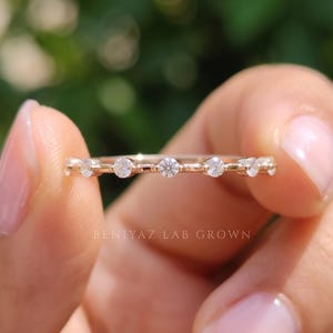 Extreme close-up of a marquise and round moissanite wedding band held between fingertips. The image highlights the brilliant faceted stones, delicate metalwork and slim stacking ring design.