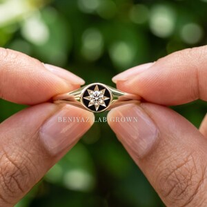 Round celestial signet ring held between fingers with champagne lab grown diamond and polished tapered gold shank