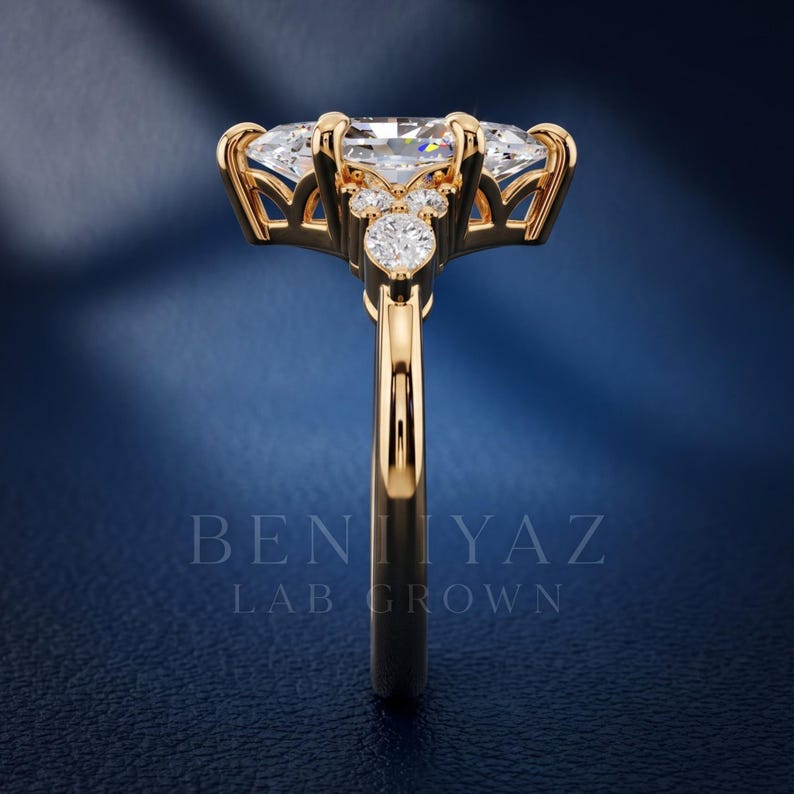 May include: A gold ring featuring a large marquise-cut center stone held by prongs, accented by smaller round-cut stones along the gallery and band. The text BENIYAZ LAB GROWN is visible in the lower portion of the image, centered below the ring.