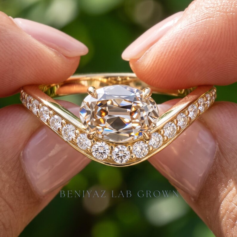 Hand displaying a yellow gold lab grown diamond engagement ring with an antique inspired design, marquise style halo, and sparkling accent stones against a natural green background
