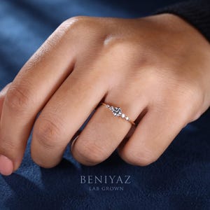 Close-up lifestyle view of a five stone lab grown diamond promise ring worn on finger, showing the petite centre stone and delicate yellow gold band.