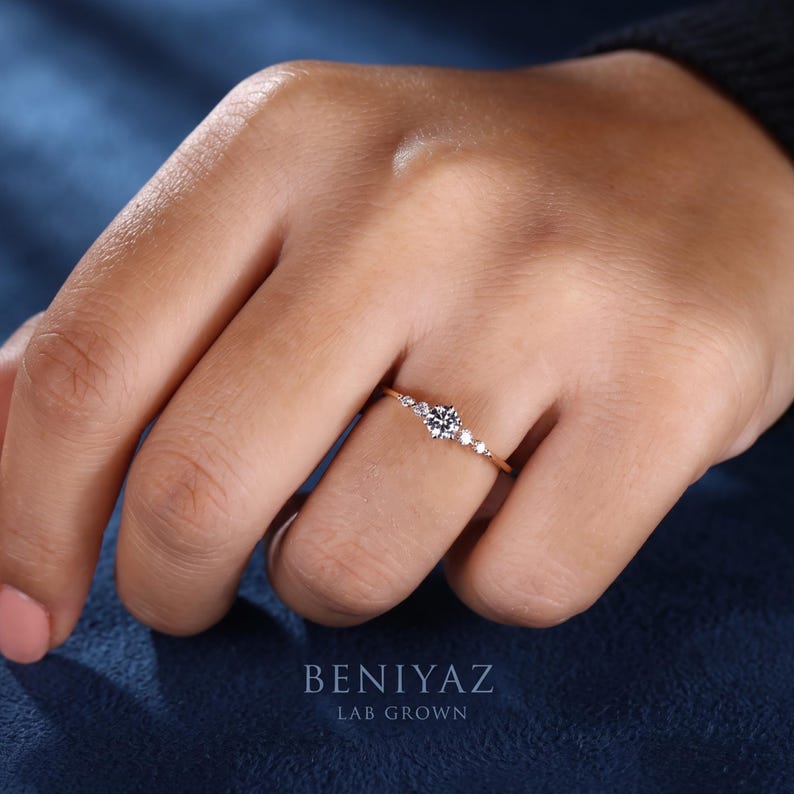 Close-up lifestyle view of a five stone lab grown diamond promise ring worn on finger, showing the petite centre stone and delicate yellow gold band.