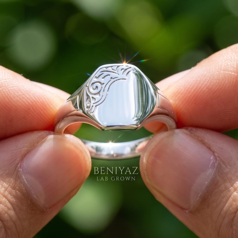 Sterling silver personalized signet ring held by hand showing blank oval engraving face and vintage floral scrollwork shoulders