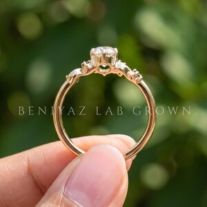 K&ouml;nnte beinhalten: Ein goldener Ring mit einem zentralen runden Brillantschliff-Stein in einer Krappenfassung und kleineren Steinen entlang der Ringschiene. Der Text BENIYAZ LAB GROWN ist mittig in wei&szlig;en Gro&szlig;buchstaben auf dem Bild zu sehen.