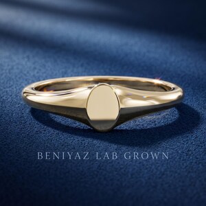 Petite oval signet ring on blue background with plain oval face, tapered shoulders and minimalist high polish finish