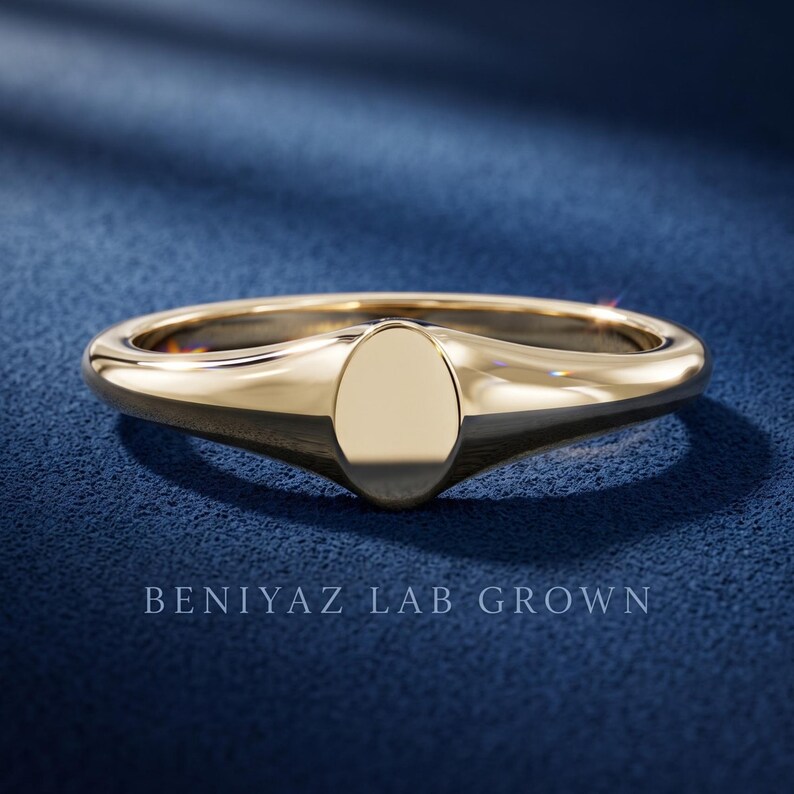 Petite oval signet ring on blue background with plain oval face, tapered shoulders and minimalist high polish finish
