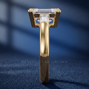 Side profile of emerald cut lab grown diamond engagement ring on blue background showing raised prong setting, open gallery and polished gold band