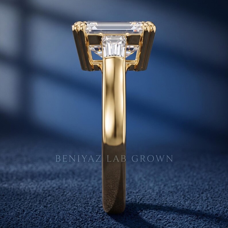 Side profile of emerald cut lab grown diamond engagement ring on blue background showing raised prong setting, open gallery and polished gold band
