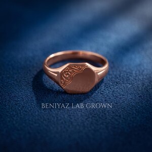 Rose gold oval signet ring on blue background with high polish face, floral scrollwork relief and tapered personalized signet design