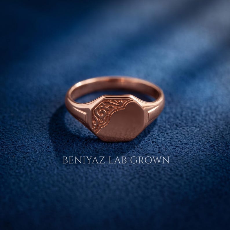 Rose gold oval signet ring on blue background with high polish face, floral scrollwork relief and tapered personalized signet design