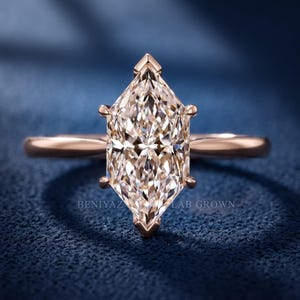 Op de afbeelding: Een ros&eacute;gouden ring met een centraal geslepen marquise-steen die door zes pootjes wordt vastgehouden. De band is glad en gepolijst. De tekst BENIYAZ LAB GROWN is zichtbaar. De steen heeft een gefacetteerd oppervlak dat licht reflecteert.