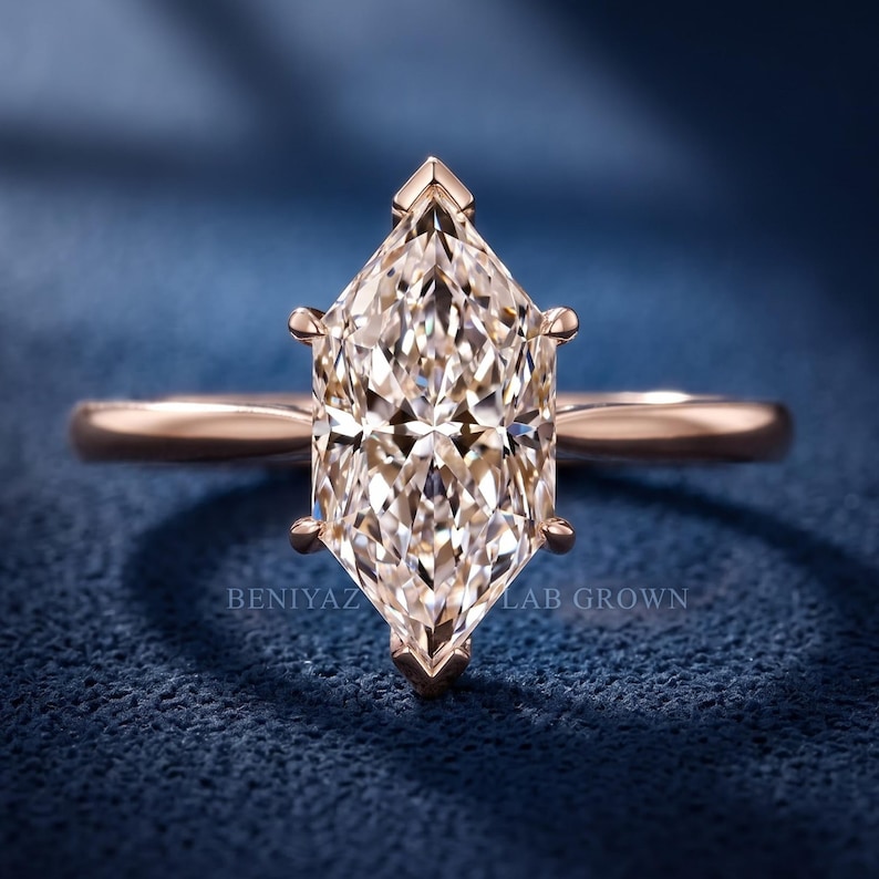 Op de afbeelding: Een ros&eacute;gouden ring met een centraal geslepen marquise-steen die door zes pootjes wordt vastgehouden. De band is glad en gepolijst. De tekst BENIYAZ LAB GROWN is zichtbaar. De steen heeft een gefacetteerd oppervlak dat licht reflecteert.