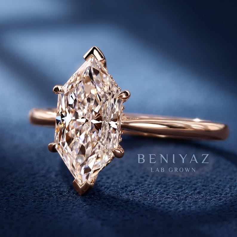 Op de afbeelding: Een ros&eacute;gouden ring met een centraal geplaatste marquise-geslepen steen, vastgehouden door zes pootjes. De ringband is glad en gepolijst. De tekst BENIYAZ LAB GROWN is zichtbaar aan de rechterkant van de ring en geeft de herkomst van de steen aan.
