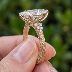 Hand held close up of a marquise lab grown diamond engagement ring with round cluster accents and pave yellow gold shoulders.
