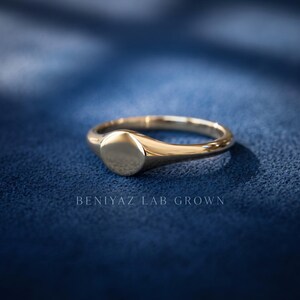 Yellow gold tone round signet ring on blue background showing tapered shoulders, slim band and smooth high polish finish