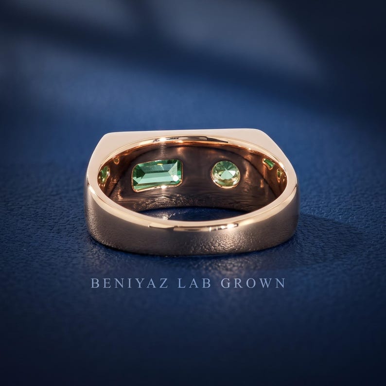 Top view of a modern teal sapphire signet ring featuring an emerald cut teal sapphire and round green sapphire in an asymmetrical two stone setting