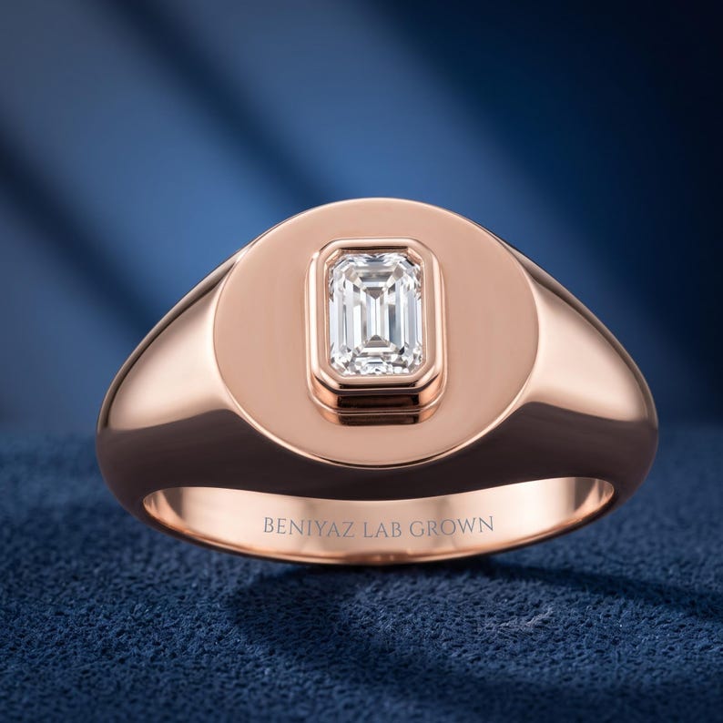 Front studio view of a rose gold emerald cut diamond signet ring with a rounded polished face and tapered shank.