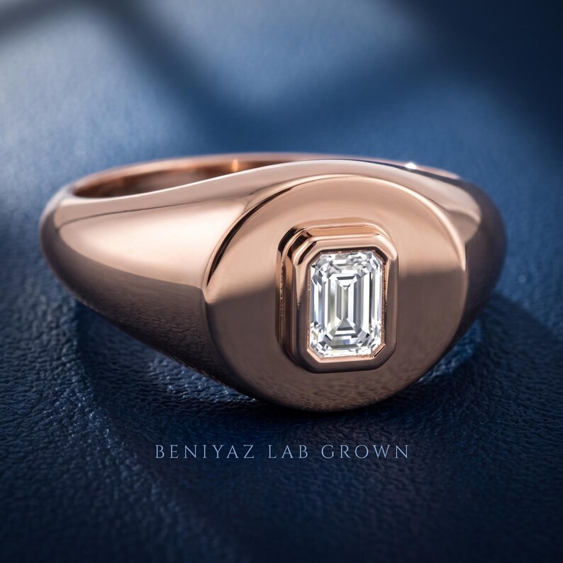 Angled rose gold emerald cut lab grown diamond signet ring on blue fabric showing the tapered shoulder profile.
