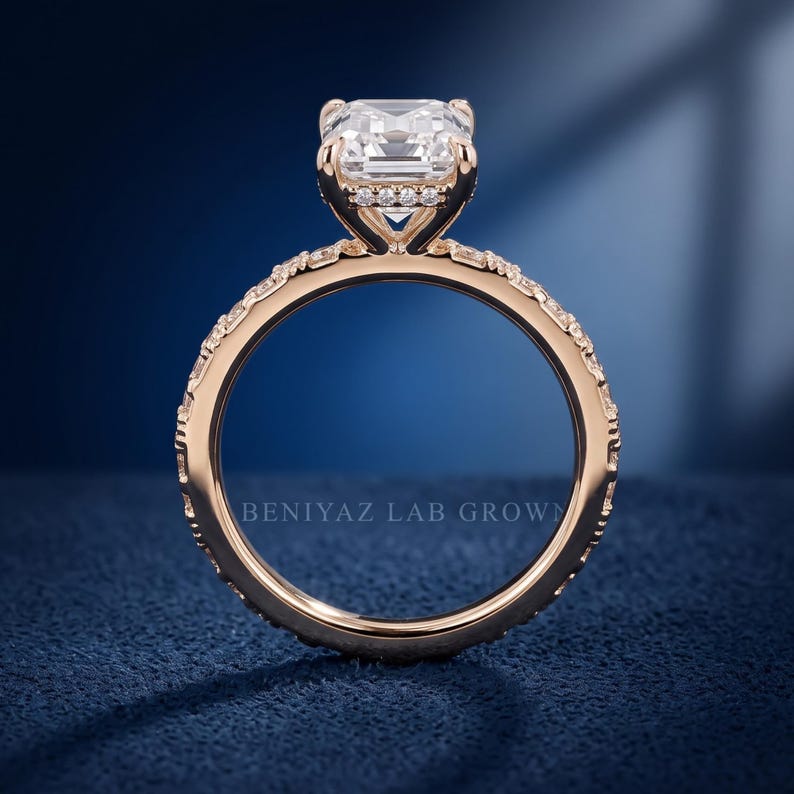 May include: A rose gold ring featuring a large emerald-cut center stone set in a basket with small accent stones. The band is pav&eacute;-set with numerous small round stones extending along the sides. The text BENIYAZ LAB GROWN is visible on the band.
