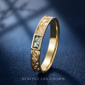 Puede incluir: Un anillo de oro con una piedra de &aacute;gata musgosa rectangular engastada en el centro. La banda est&aacute; decorada con un patr&oacute;n de hojas en relieve en los laterales. El texto BENIYAZ LAB GROWN aparece impreso en la parte inferior en letras blancas.