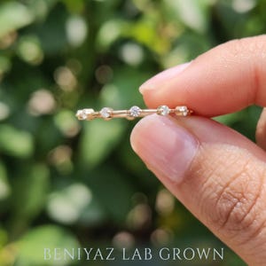 Side view of a dainty moissanite wedding band held between fingertips, highlighting the marquise shaped stones, round accents, polished metal setting and elegant low-profile design.