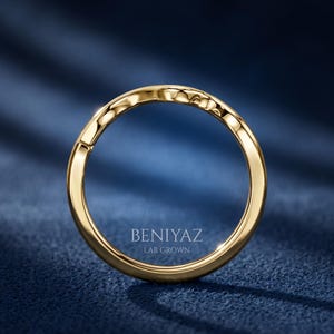 Angled close up of a minimalist yellow gold wishbone wedding band showing its smooth curved nesting design.