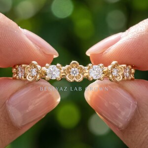 May include: A gold band ring featuring alternating round clear stones and five-petaled flower-shaped settings with central clear stones. The text BENIYAZ LAB GROWN is printed in white across the center of the ring. The design is symmetrical.