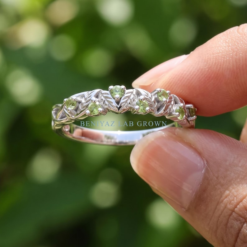 Peridot stacking ring with botanical leaf and vine design, polished metal finish and round green gemstones.