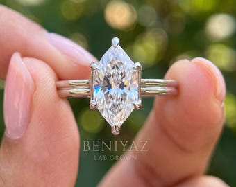 May include: A silver-toned ring featuring a large, marquise-cut, clear center stone held by six prongs. The band is composed of two parallel metal bars. The text BENIYAZ LAB GROWN is printed in white on the lower portion of the image.