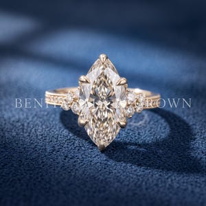 Front angled view of a 3 CT marquise diamond engagement ring in yellow gold on a dark blue luxury background.