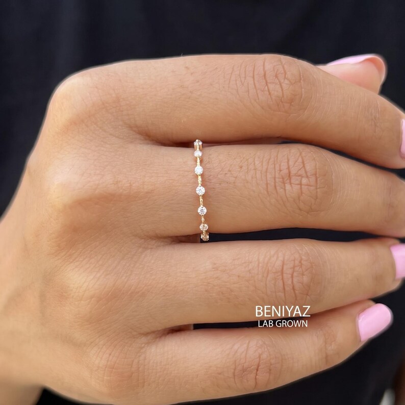 Elegant hand wearing a delicate moissanite stacking ring with marquise and round stone accents. The slim wedding band is photographed in natural light with soft pink nails and a neutral outfit.