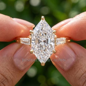 2 carat Dutch marquise lab grown diamond engagement ring held between fingers with elongated F VS1 center and side stones
Marquise diamond ring with a 2 carat Dutch marquise lab grown diamond and small side diamonds on a slim gold band