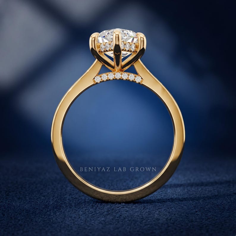 Hand held rear view of a marquise engagement ring showing the polished yellow gold band and elevated hidden halo setting.