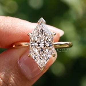 Op de afbeelding: Een ring met een diamant in marquise-slijpvorm, gezet in een gepolijste geelgouden band. De centrale steen heeft een gefacetteerde, langwerpige vorm en wordt vastgehouden door zes pootjes. De tekst BENIYAZ LAB GROWN is zichtbaar op de zijkant.