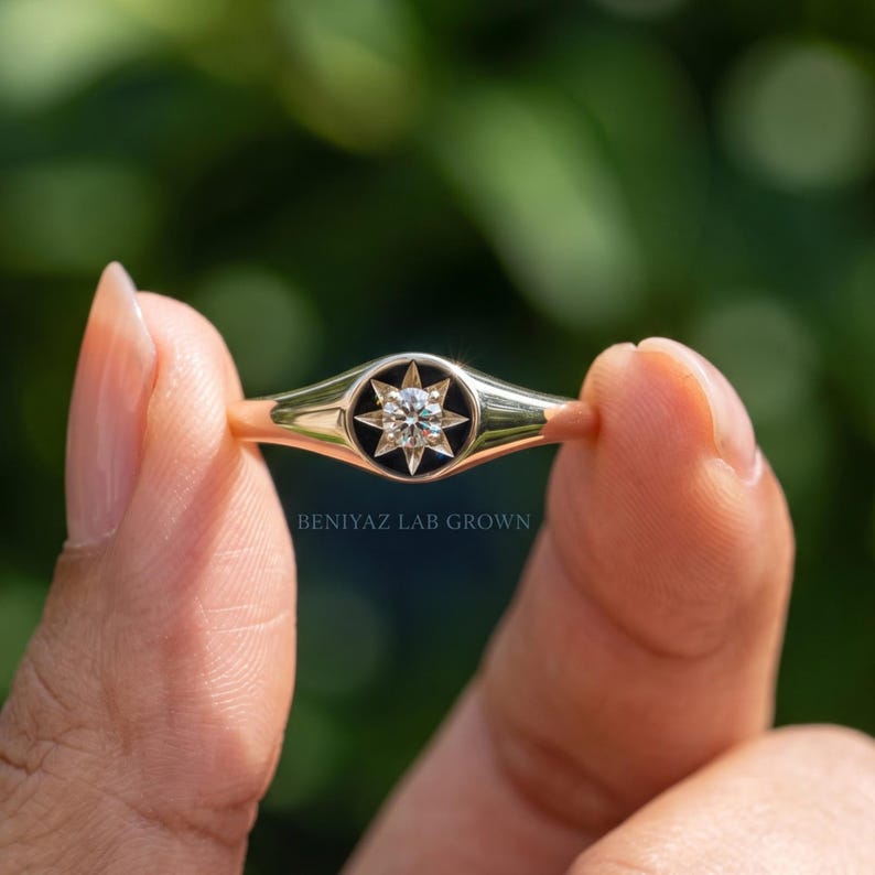 Round celestial signet ring held between fingers with champagne lab grown diamond and polished tapered gold shank
